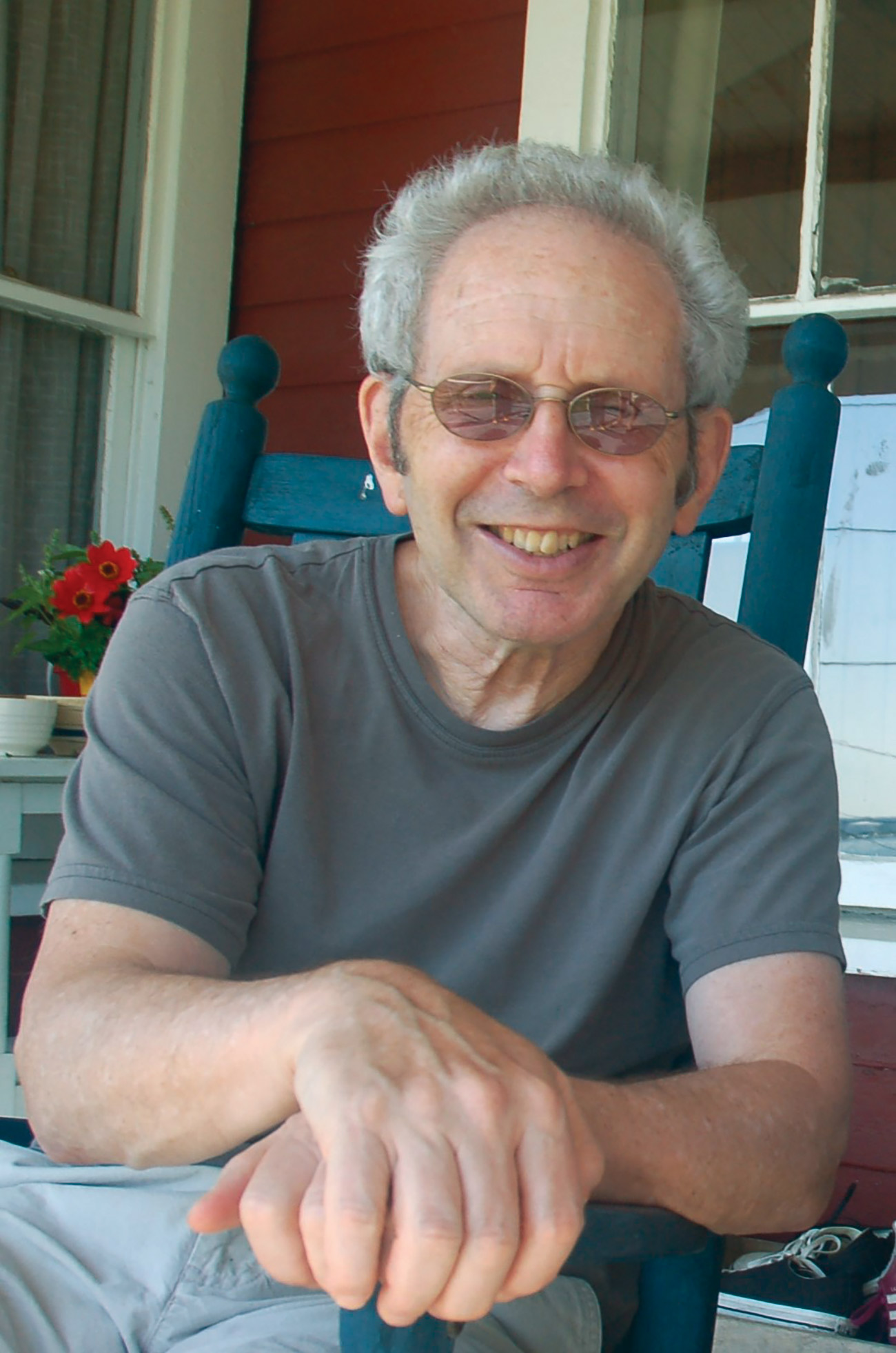 Photo of Peter Guralnick with glasses on sitting in a teal rocking chair on a porch.