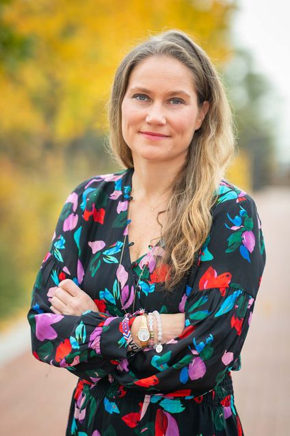 Photo of Annie Tomasini with a colorful, floral blouse on with her arms crossed, smiling.