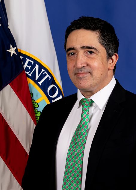 Headshot of Ramin Taheri in a green tie and suit, in front of an American and DOE flag.