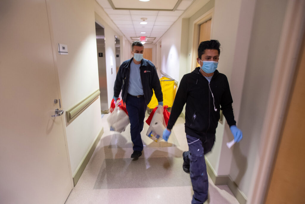 A photo of Carlos Carreiro and Andres Lopez delivering paper goods to an empty quarantine room on Comm Ave. 