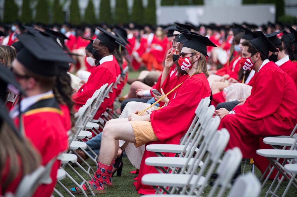 A graduate wearing shorts beneath his robe has his legs and red BU Terrier socks exposed.