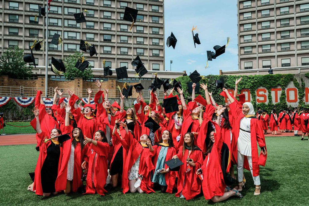 A group of graduating students pose for a photo and throw their graduation caps up in the air.