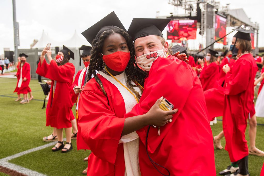 Two graduates, masked, hug each other