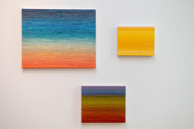 Photo of three paintings by Cailyn Masson (CFA’21) on view in the BFA Thesis Exhibition. The paintings are of various sizes and feature stripes of pastel colors that resemble sunsets.