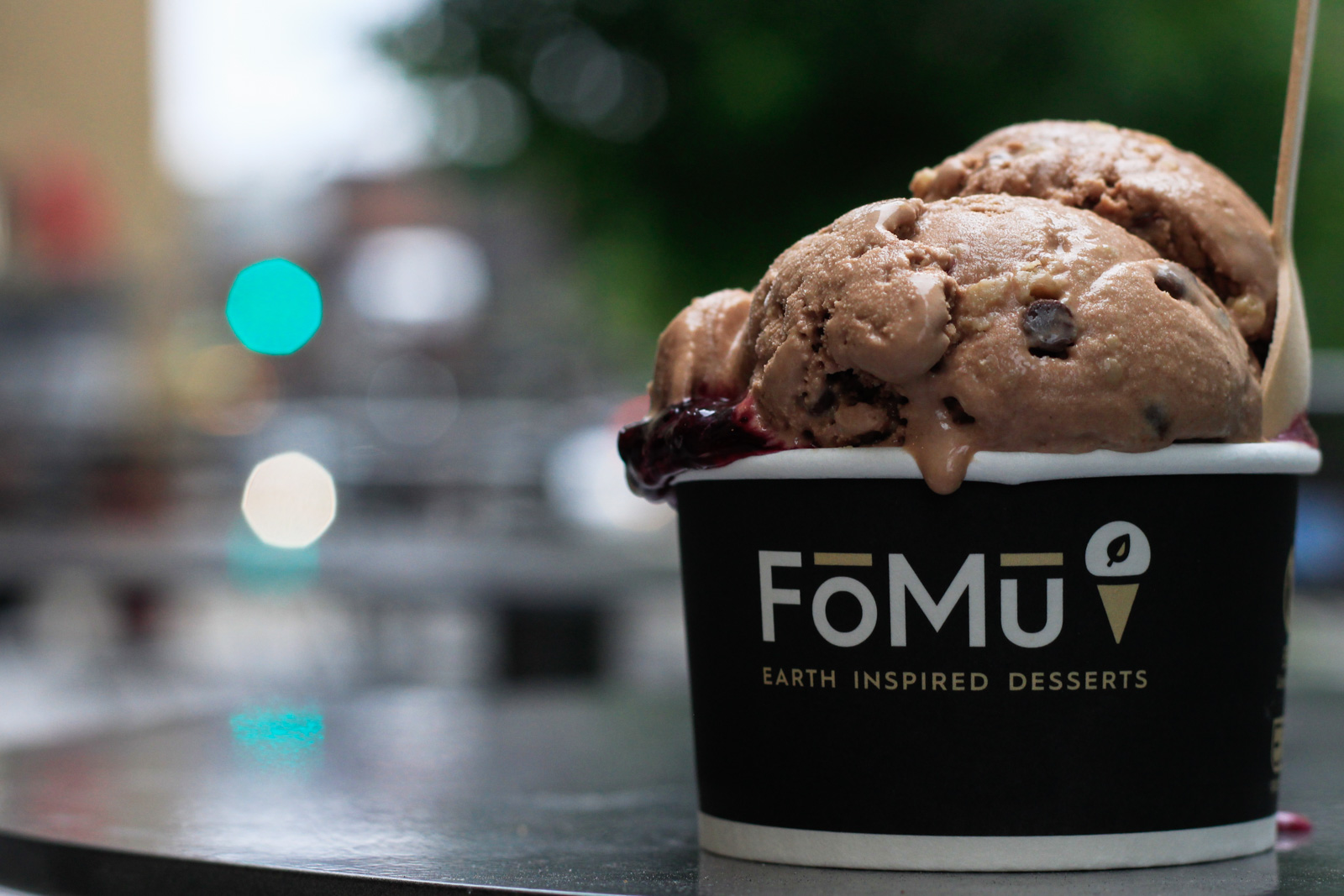 A large scoop of FoMu vegan chocolate cookie dough ice cream in a cup sits on a table in the FoMu vegan ice cream shop in Allston.