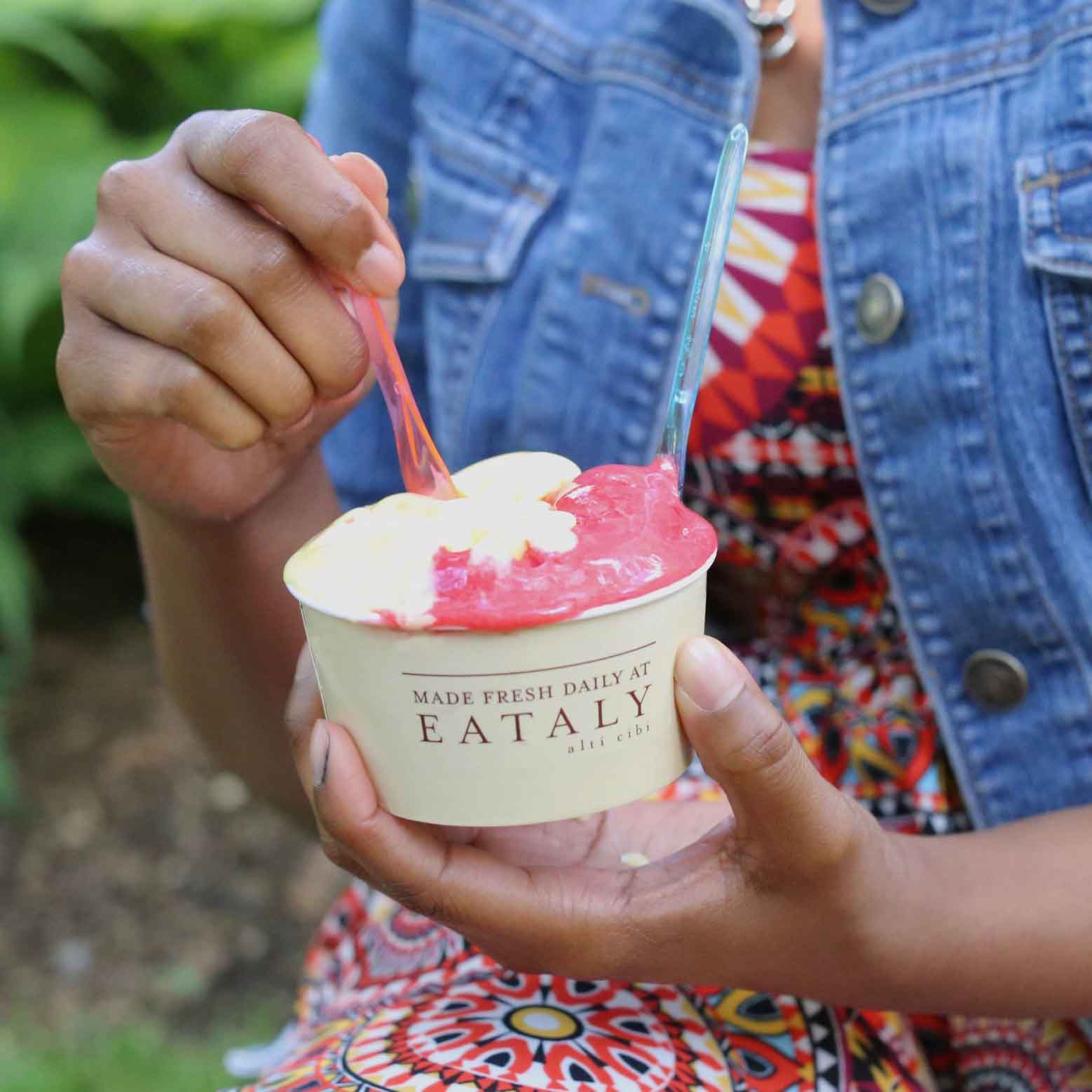 A woman in a patterned dress and jean jacket eats a cup of gelato from Il Gelato.