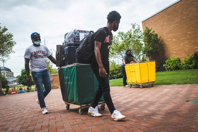 Photo of a student and possibly his father walking with a green moving build filled high with his belongings.