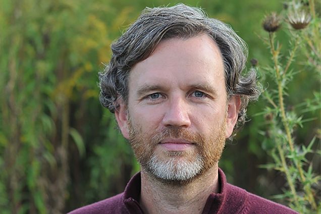 Headshot of David Jones wearing a maroon pull over and standing in front of some greenery. He slight smiles and has salt-and-pepper hair.