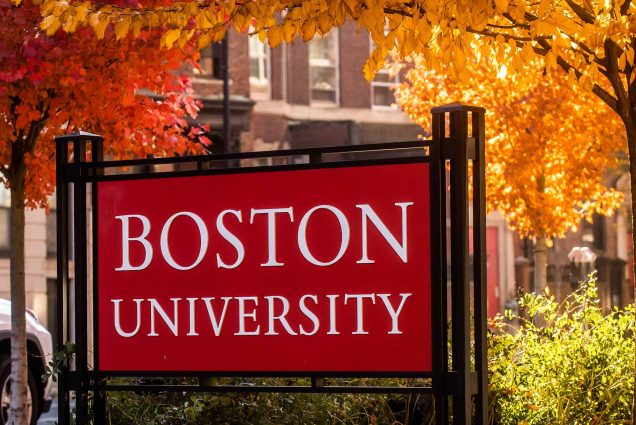 a photo of a red sign that reads "Boston University" surrounded by trees with red and orange fall leaves.