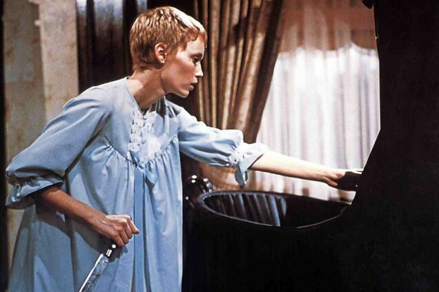 Still from the horror film Rosemary's baby. Rosemary stands in a blue night gown with a knife in her hand over a black baby cradle.