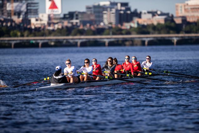 Photo of the women's rowing team on the Charles. Behind them, a bridge and the Citgo sign is seen.