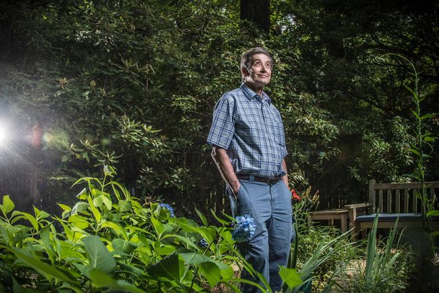 Neuroscientist Stephen Grossberg standing in his yard looking up at the sky with a light shining behind him.