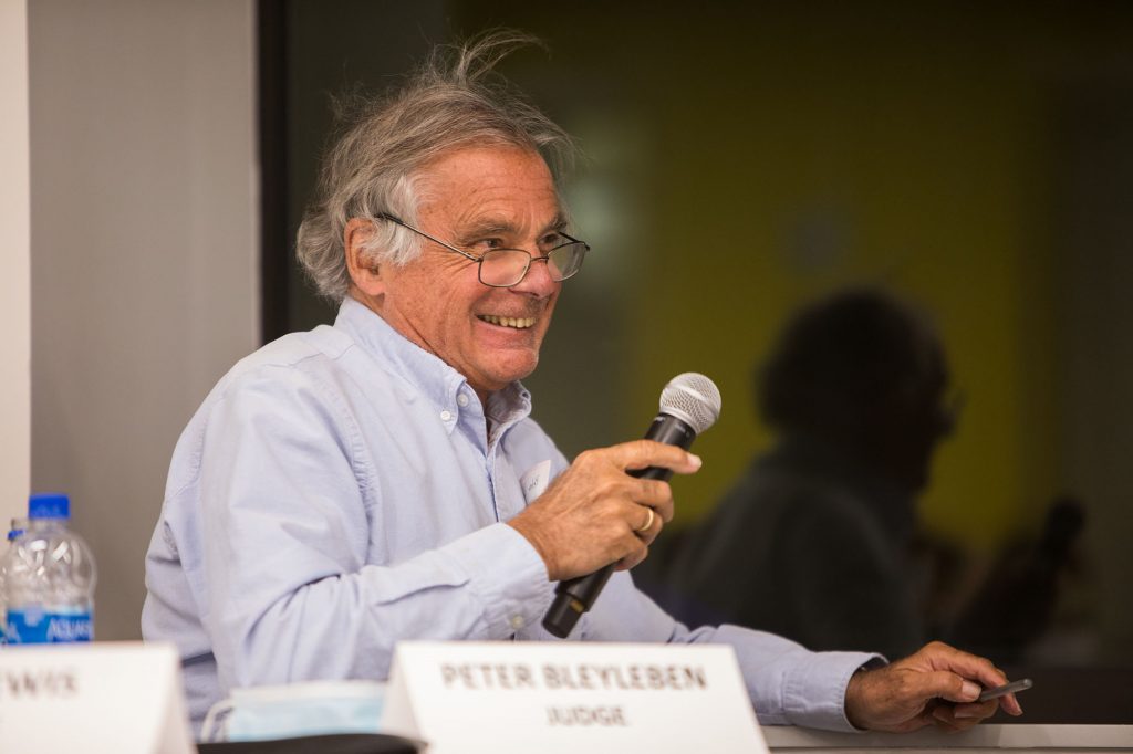 Candid photo of Peter Bleyleben, a partner in Converge Venture Partners, who was one of this year’s competition judges. He sits with microphone in hand, wearing a blue collared shirt. A nameplate with his name on it is placed before him.
