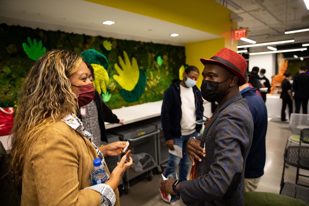 photo of Cannabis Start-Up Competition finalist Michelle Matsuba presenting on Eleganja, a platform that supports Black-owned cannabis companies. She is masked and speaks to another masked, black person wearing a red cap in the BUild lab.
