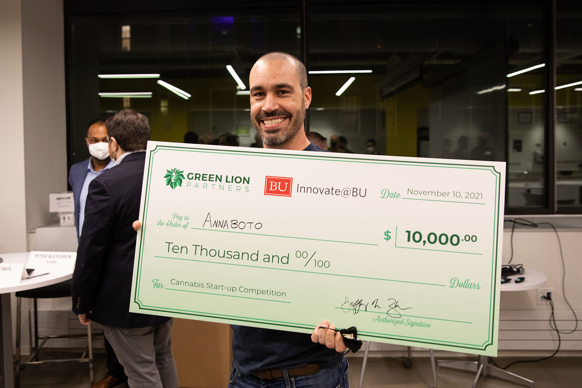 a photo of Carl Palme, the winner of the Innovate@BU and Green Lion Partners annual Cannabis Start-Up Competition. He smiles as he holds a giant, light green check for $10,000.