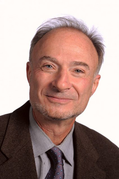 headshot of Jeremy Yudkin, a CFA professor of music. He wears a dark brown blazer over a light grey collared shirt and smiles at the camera.