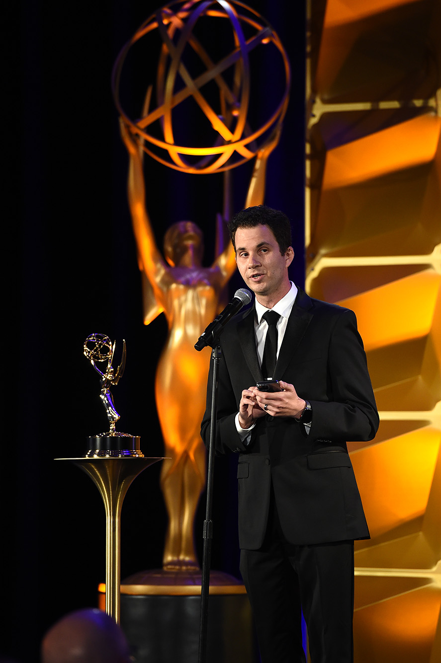 photo of Steve Vitolo of Scriptation accepting his Emmy at the 73rd Engineering Emmy Awards, presented by the Television Academy on October 21, 2021, in Los Angeles. He wears a black suit and speaks into a microphone as a large Emmy statue is featured in the background.