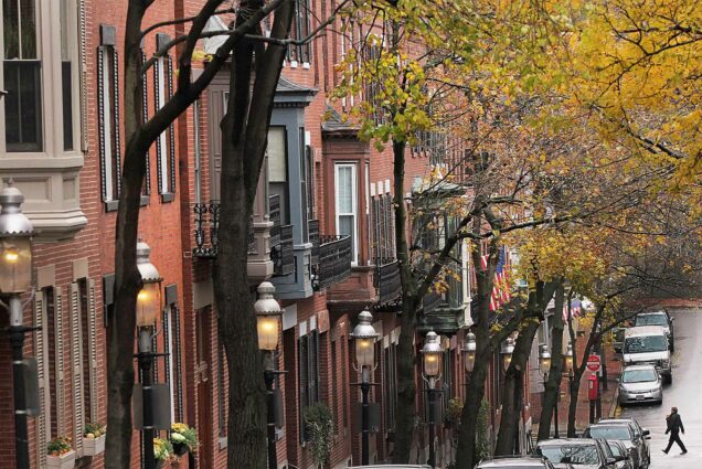 multiple Charlestown brownstones stand in a row with fall leaves on tress in the foreground