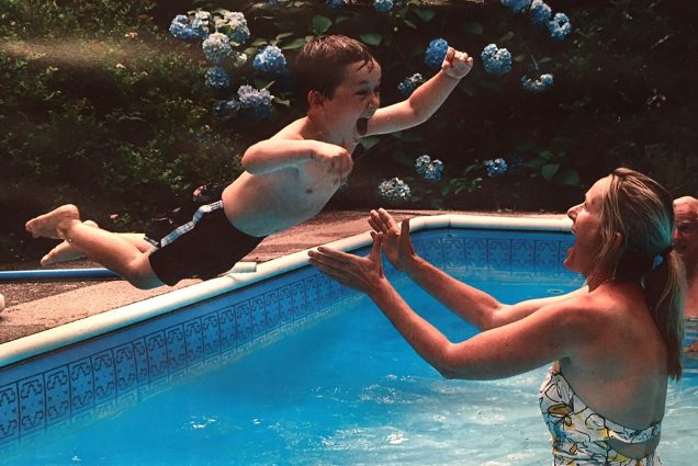 a photo of Scarlett Lewis (COM’20), with her son Jesse a few months before his death in the Sandy Hook shootings. He is mid-jump into her arms as she stands in a pool wearing a white floral bathing suit.