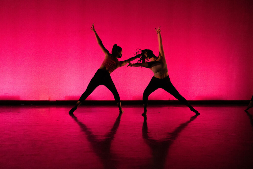 Two dancers pose against a red/orange background on a stage