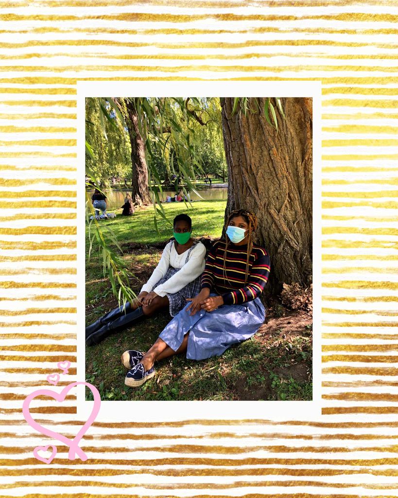 Photo of Khloe Katende (CGS’20, COM’22) and her friend sitting under a willow tree in what looks like Boston Public Garden. The photo is overlaid on a white and gold striped background and a few pink hearts are drawn over the background and photo.