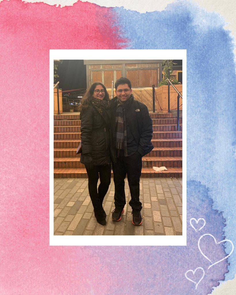 Photo of Dhruv Raman and their partner in winter clothing standing outside with their arms around each other. The photo has a white border, similar to that of a polaroid, and is on a background with a pink and blue watercolor blob. A few white hearts are overlaid at the bottom.