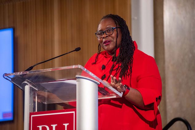 Photo of Dr. Angela Onwuachi-Willig - Dean of Ryan Roth Gallo & Ernest J. Gallo Professor of Law, BU School of Law at the SDO speaking at the podium during the Critical Race Theory (CRT) panel at Howard Thurman Center Feb 10. AOW wears a red jacket and has shoulder length locs.
