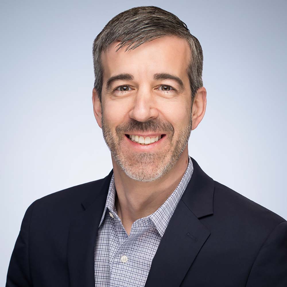 Portrait of LAW’s John Beccia, a middle aged white man who smiles, has short salt and pepper hair and wears a dark blue suit jacket.