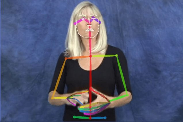 Screenshot of a woman signing. Her face and body are outlines by colorful lines showing how AI might recognize the signs she makes.