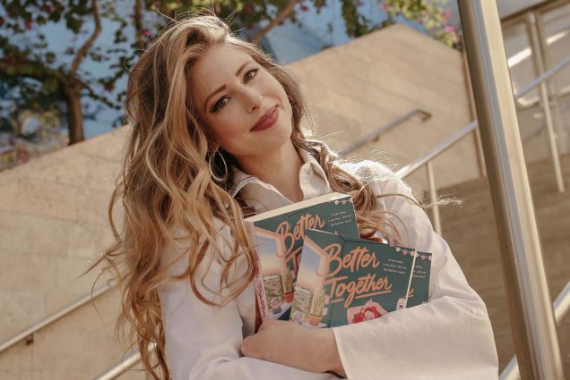 Photo of Christine Riccio (COM’12) sitting on a cement staircase outside and hugging three copies of her book "Better Together." Riccio has long, wavy blonde hair and tilts her head as she smiles. She wears a white blouse with white sleeves and tan corduroy overalls.
