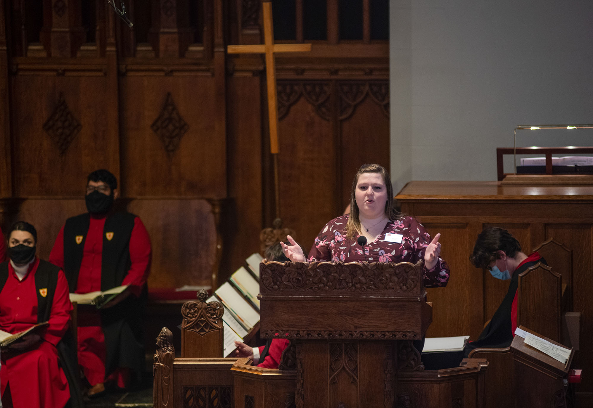 Photo of Chloe McLaughlin standing with hands wide as she stands at a wooden podium in Marsh Chapel.
