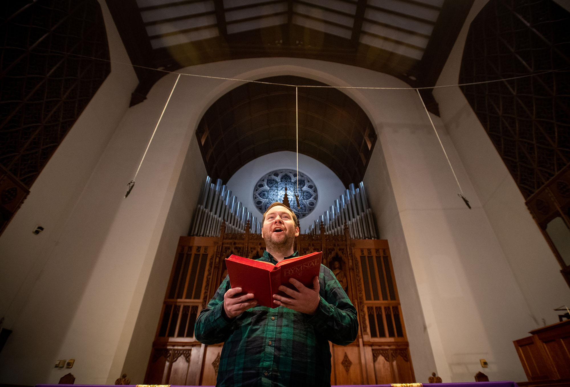 Photo of Kristian, a white man wearing a dark green and black plaid shirt, singing in the Marsh Chapel choir.