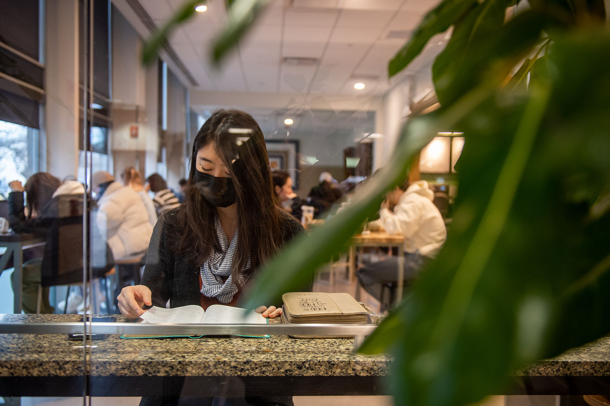Photo of Mary Choe (CAS’24), an Asian woman wearing a black mask, as she reads her daily scriptures in a cafe