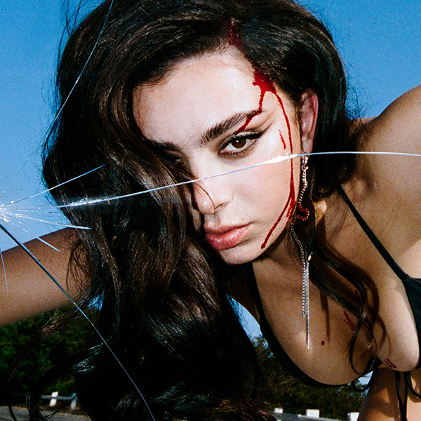 Album cover of Charlie XCX's album "Crash". Image shows Charlie XCX, a white woman with black hair wearing a black bikini swim suit, on the hood of a car peering at the camera as if looking into a windshield. The windshield glass is cracked and the woman is bleeding from her forehead