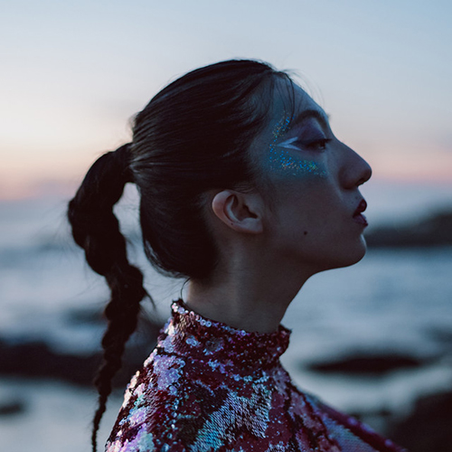 Album cover for Haru Nemuri's "Sunka Ryougen". Cover is a profile photo of Nemuri as she wears silver, glittery eye makeup, and elaborate Japanese red dress, and looks to the right as ocean waves can be seen in the background.