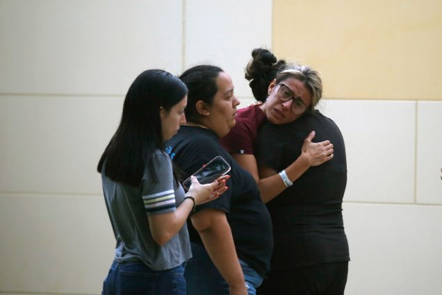 Photo of the members of the community of Uvalde, Tex., mourning after a deadly school shooting at Robb Elementary School. In the photo, four women presumably Latinx women are seen, mostly from the side. One woman hugs another, her face is filled with tears. She has blonde hair and wears glasses.