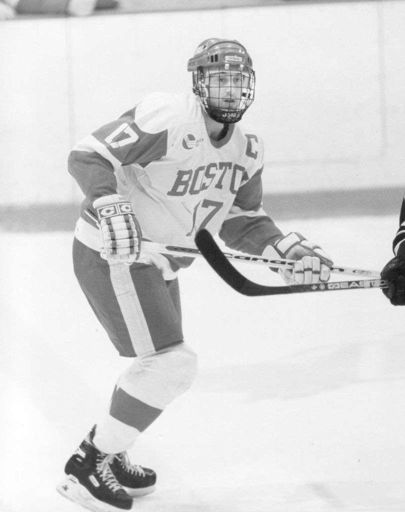 Black and white photo of Jay Pandolfo skating as a terrier in the late 90s. He wears number 17, and holds a hockey stick up during a game.