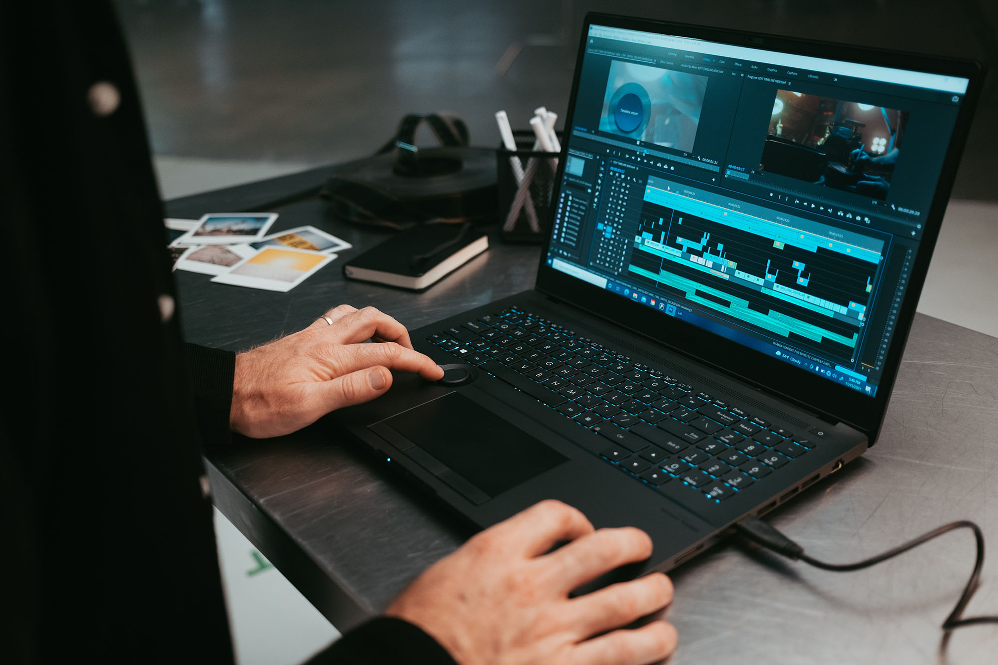 Photo of someone editing a video using video editing software on their laptop. Two hands and the laptop screen are seen as they work on a metal table.