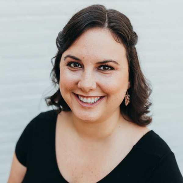 Photo of Sarah Prager, a white woman with short brown hair. She wears a black, short-sleeved shirt and smiles at the camera.