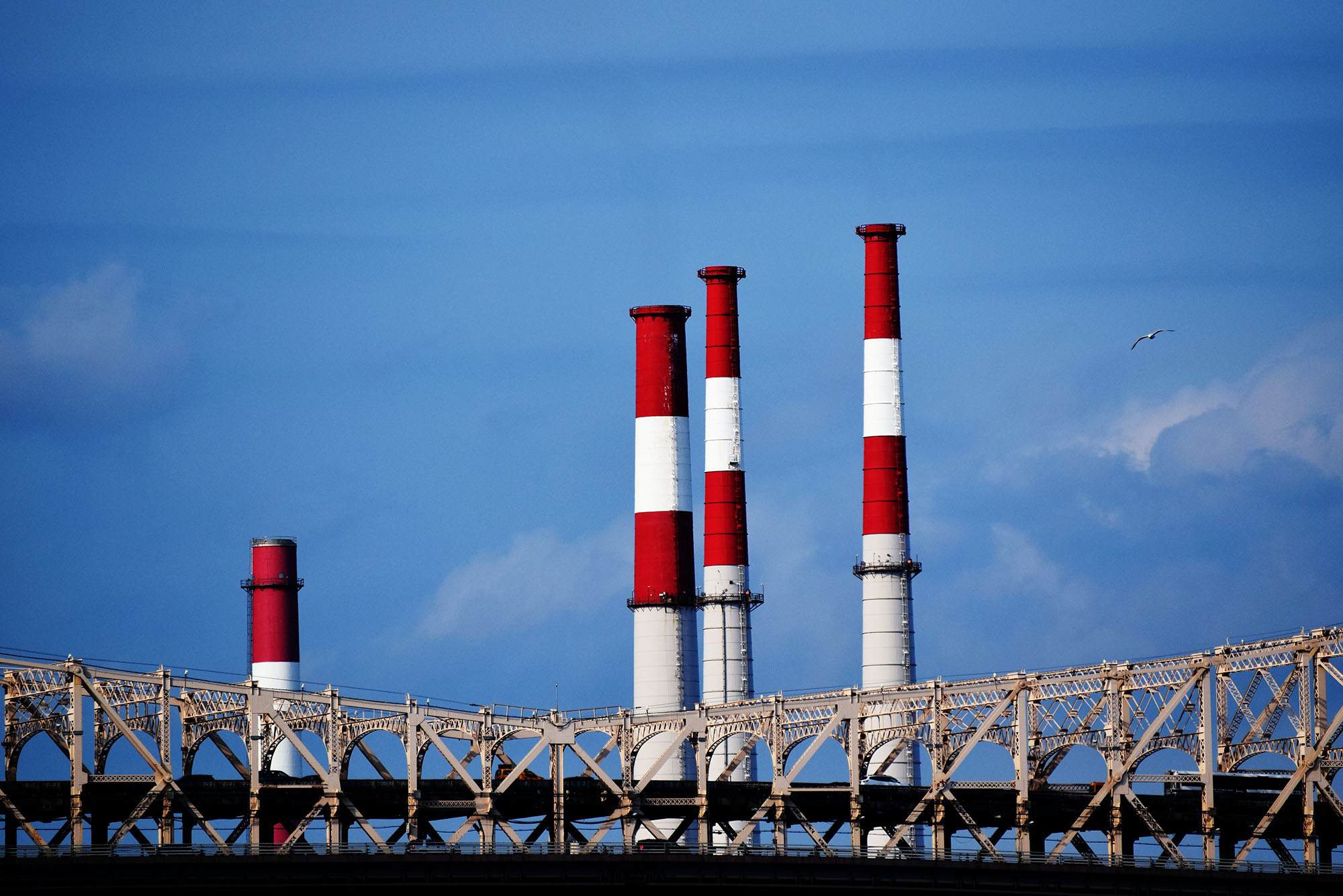 Photo of three red and white smokestacks looming behind a bridge on a clear, blue day