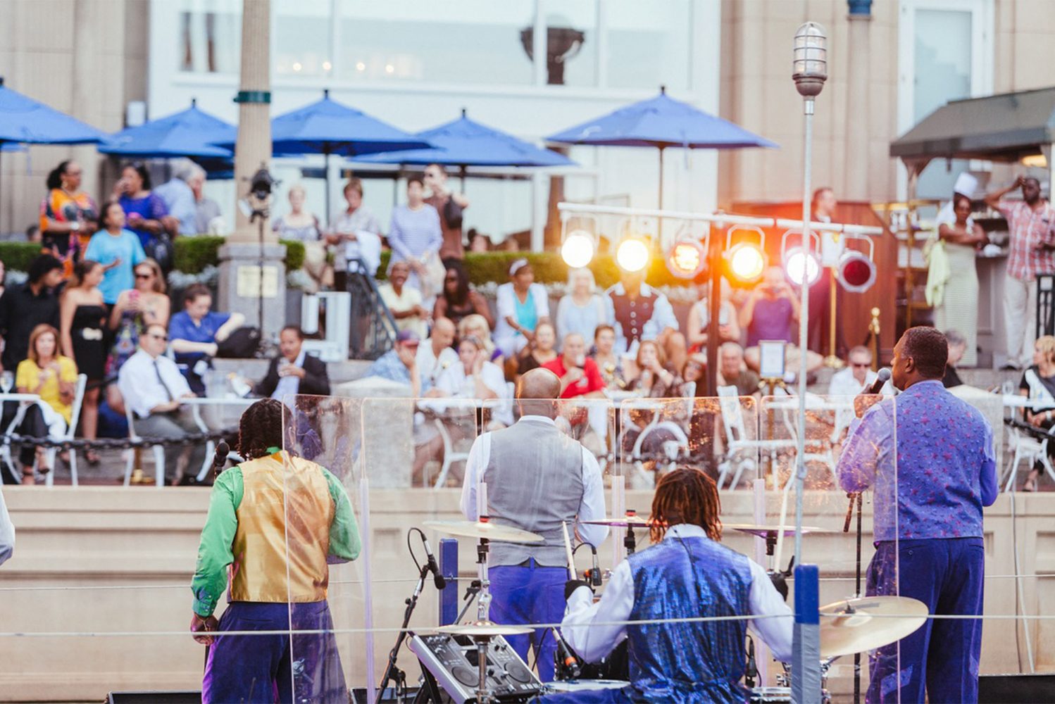 The Boston Harbor Hotel, home of the Harborwalk Terrace restaurant, is hosting live music during its Summer in the City events. Photo courtesy of the Boston Harbor Hotel. In this photo a band of men in blue and white shirts play for a crowd near Boston Harbor