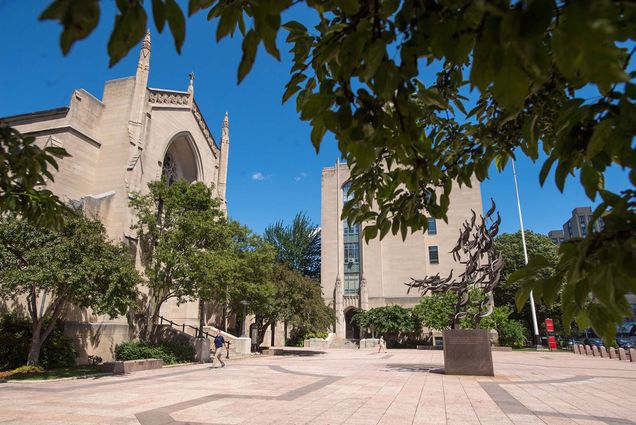 Photo of BU's campus. Image shows Marsh Plaza with green trees and a metal sculpture in the center.