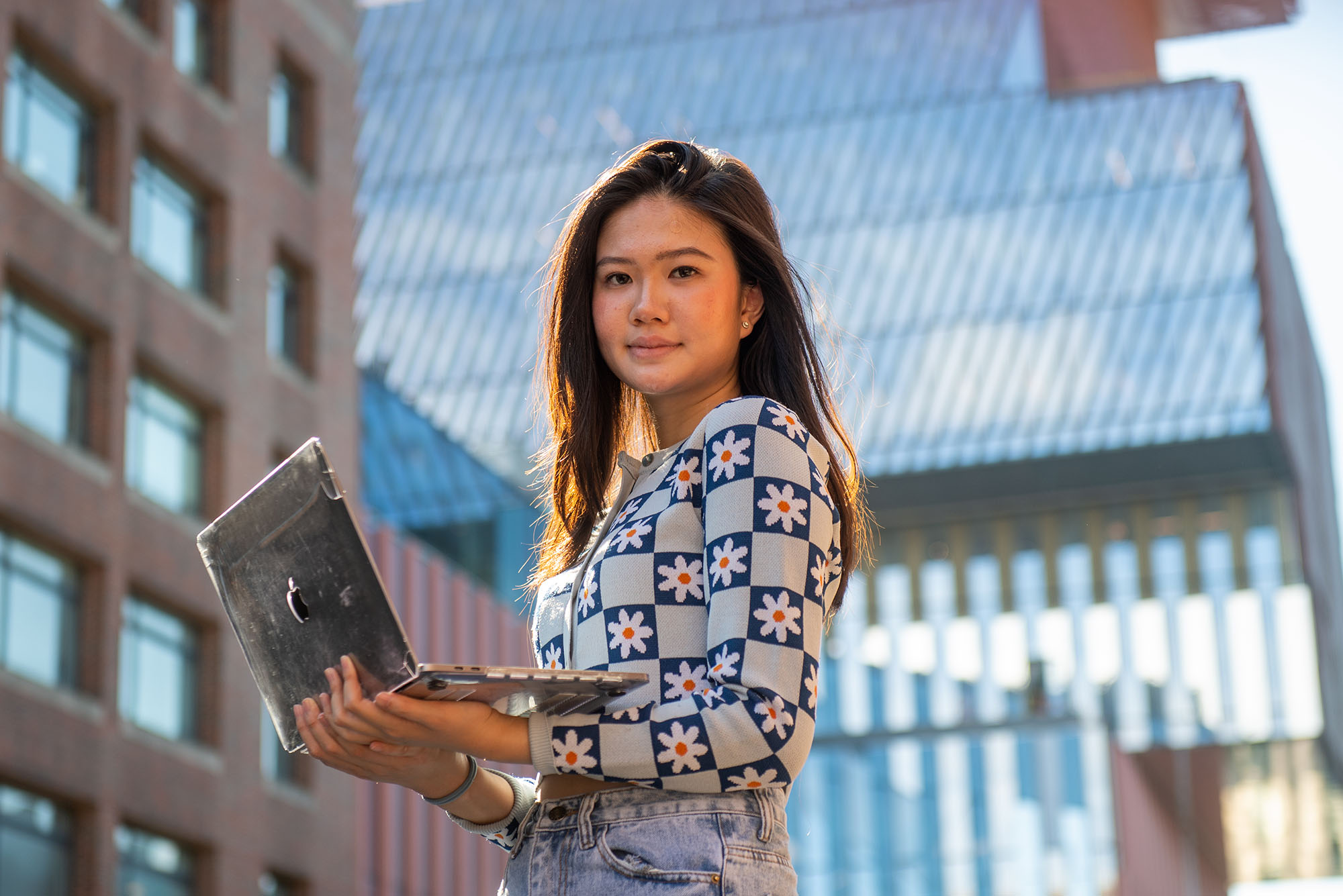 Photo of Selina J. Manua. A young, South east Asian woman holds a laptop in front of her as she poses in front of the BU Data Sciences building.