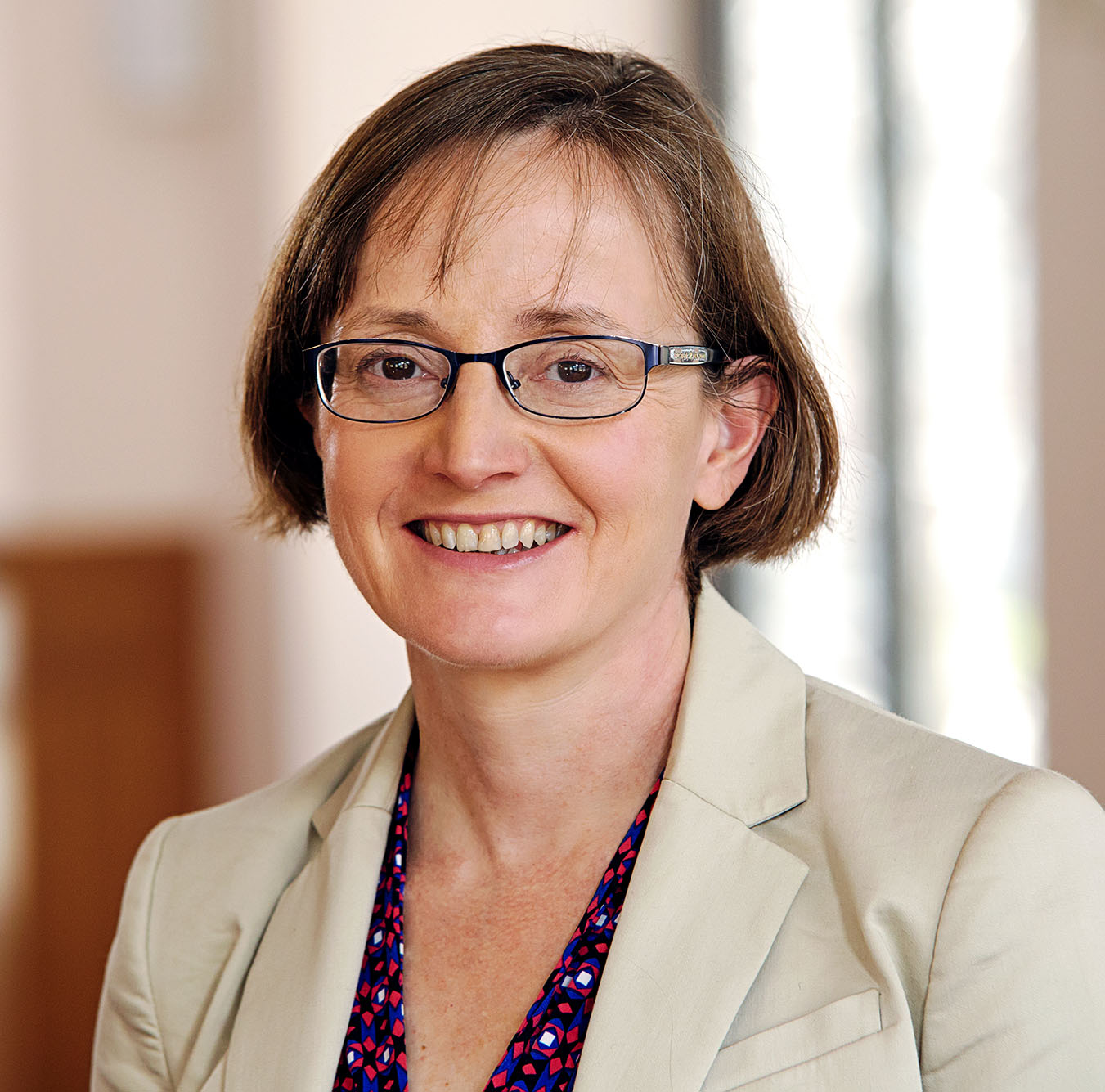 Headshot of Margaret Martonosi. A white woman with short, auburn hair wearing glasses, a tan blazer, and a burgundy floral printed blouse smiles to the camera.