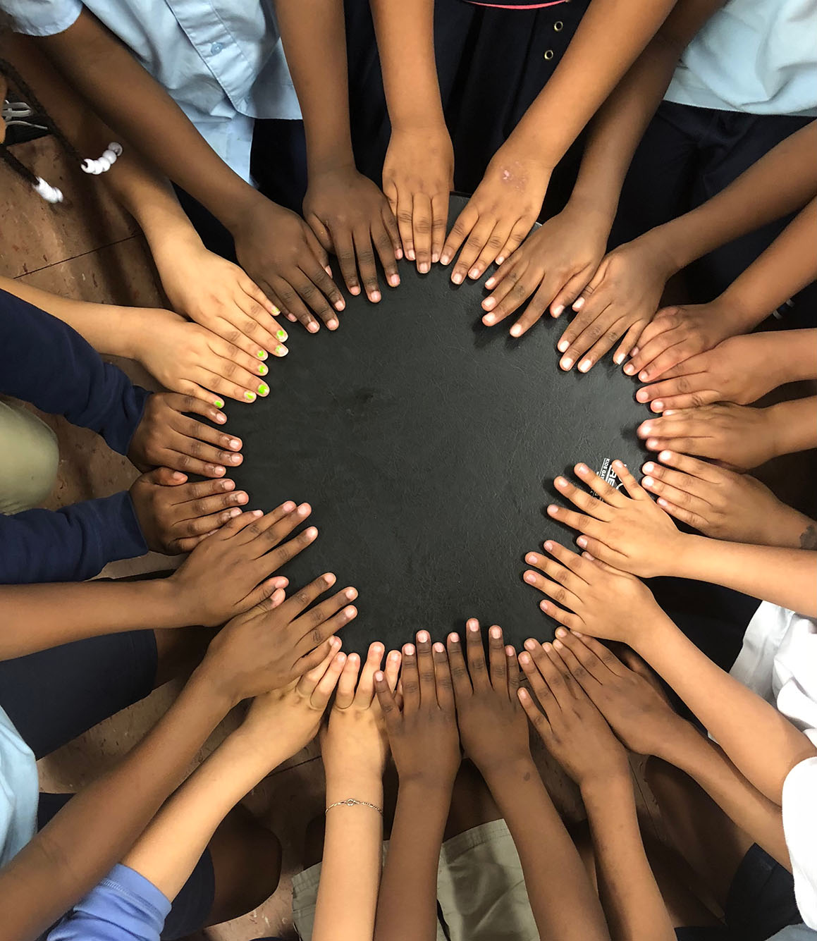 Photo: A group of children's hands form a circle. Hints of a light blue uniform can be seen on the children.