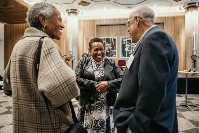 Photo of Katherine Kennedy (center), talking and laughing with hands clasped in front of her. Andrea Taylor stands to her left and Professor Roscoe Giles stands to her right.