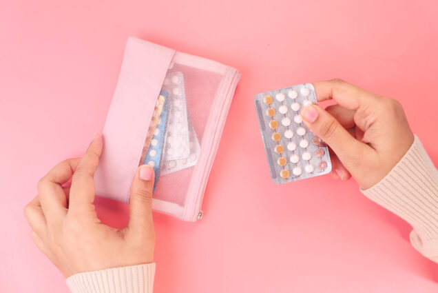 Photo of a person holding birth control pills close up. They hold a pack of slightly used pills over a pink background.
