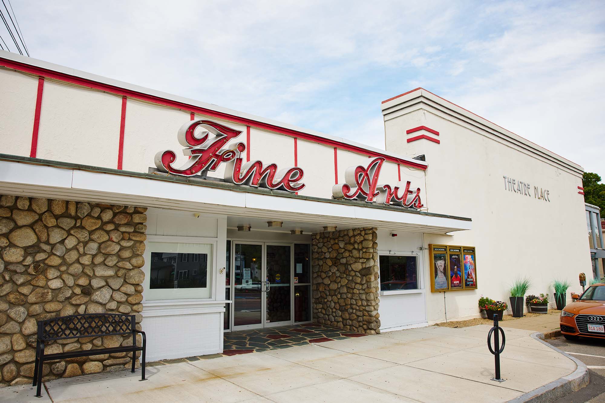 Photo of a small theater. A white building with red embellishments is shown. A large red sign that reads "Fine Arts" stands atop.