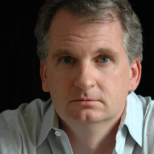 Photo: Headshot of Timothy Snyder. A white man with silver grey hair and wearing a white collared shirt poses against a dark background.