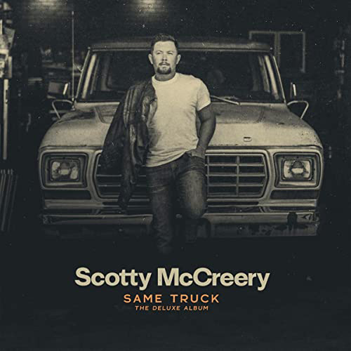 Album Cover of "Same Truck: The Deluxe Album" by Scotty McCreery. McCreery stands in front of an old truck in this black and white photo.